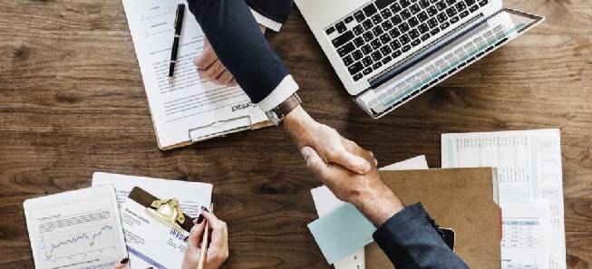 Two gentlemen giving a handshake to each other on a table after their company registration.