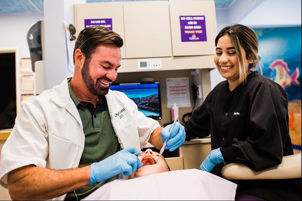 A dentist and his assistant are examining patient's teeth with dental probe and dental mirror before large dental equipment.