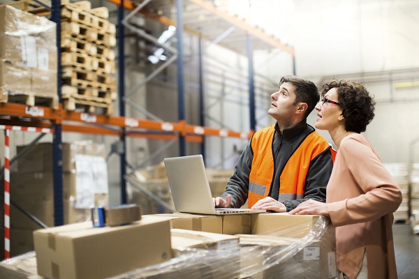 Managers of a warehouse working on a laptop and supervising the stock in the shelves.